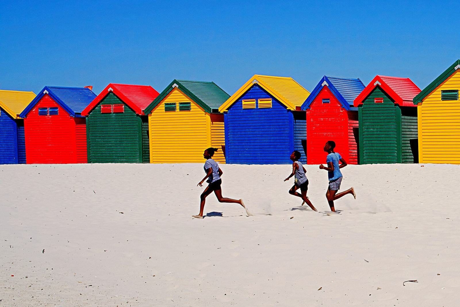 Children running on a beach in front of colourful beach huts